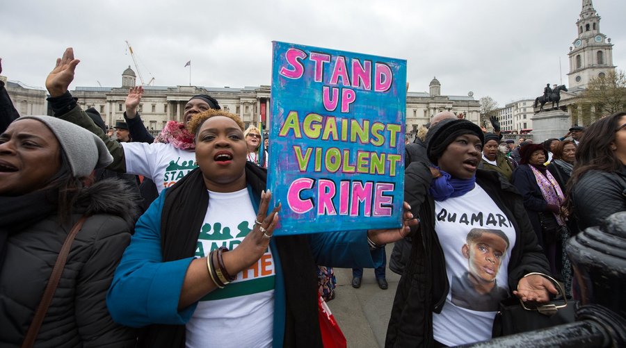 Two women at a protest, holding up a sign saying "stand up against violent crime"