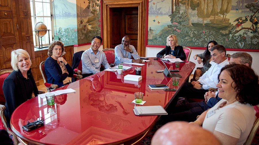 A group of smiling people seated around a table in the Red Salon of Schloss Leopoldskron.