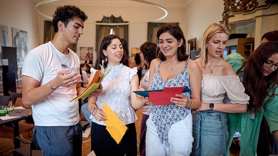 four individuals stand next to each other engaged in conversation and holding colored papers