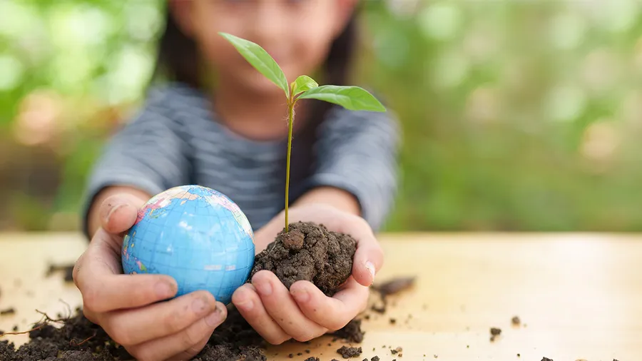 a girl holds a globe and plant.
