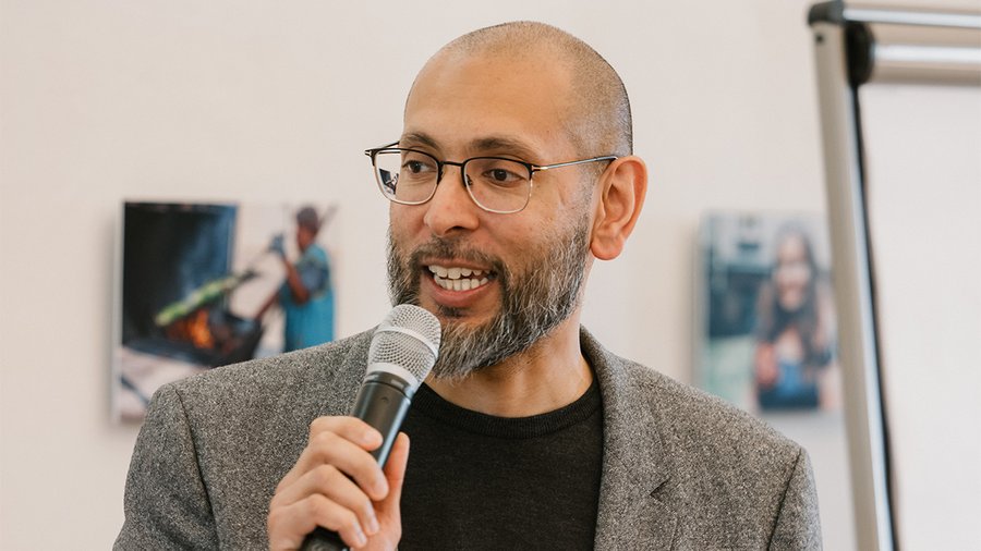 A man speaks into a microphone while looking to the left