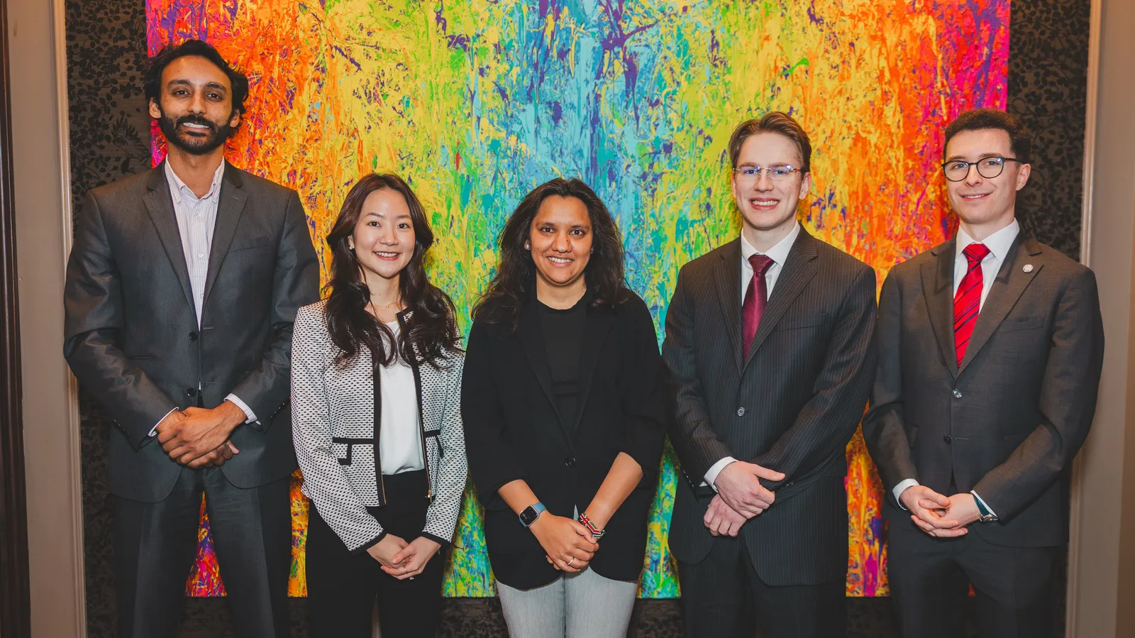 a group of individuals smile and pose for a picture in front of a colorful background