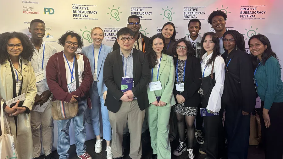 a group of young diverse people wearing professional clothing in front of a sign reading "creative bureaucracy festival"