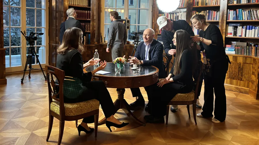 Marion Gehlert, Oleksandra Matviichuk, and Martin Weiss on the set of München.tv. These three people sit around a table during a discussion in a library.