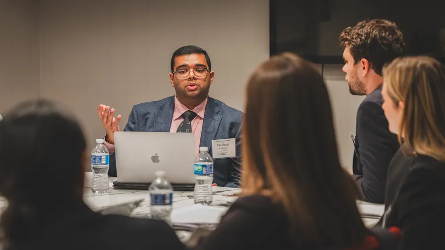 a man speaks at a table with other people listening to him