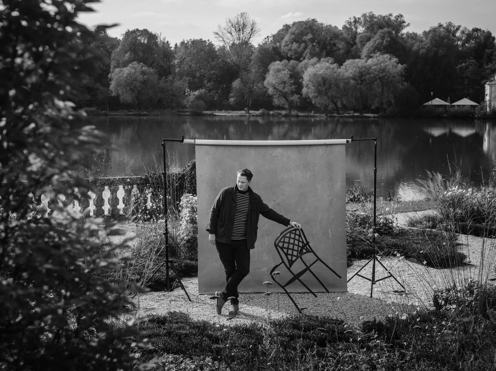 Black-And-White Photo of a Man Holding a Chair at an Angle, With the Castle Pond in the Background