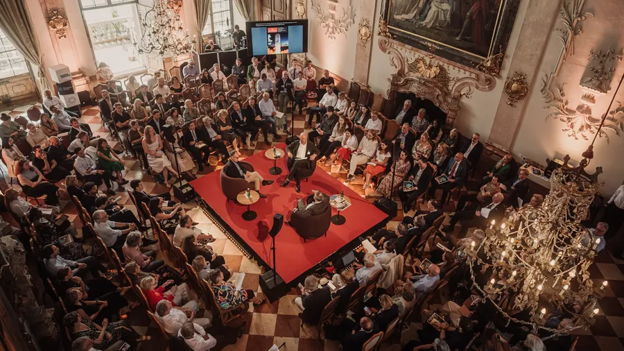 the Marble Hall of Schloss Leopoldskron is filled with people sitting around a stage in the center
