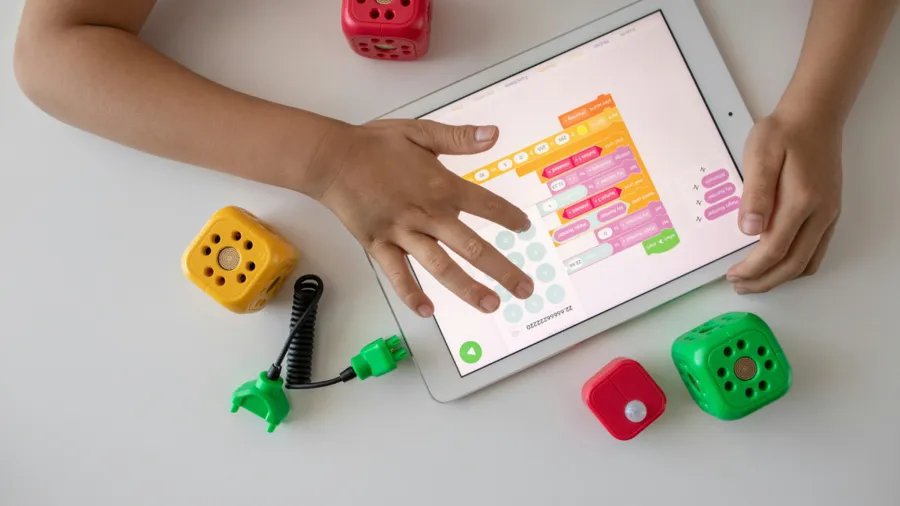 a photo taken from above of a child's hands using a digital tablet with some toys nearby
