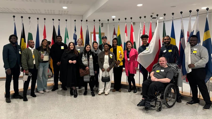 A group of people stand smiling and posing in front of a row of flags.