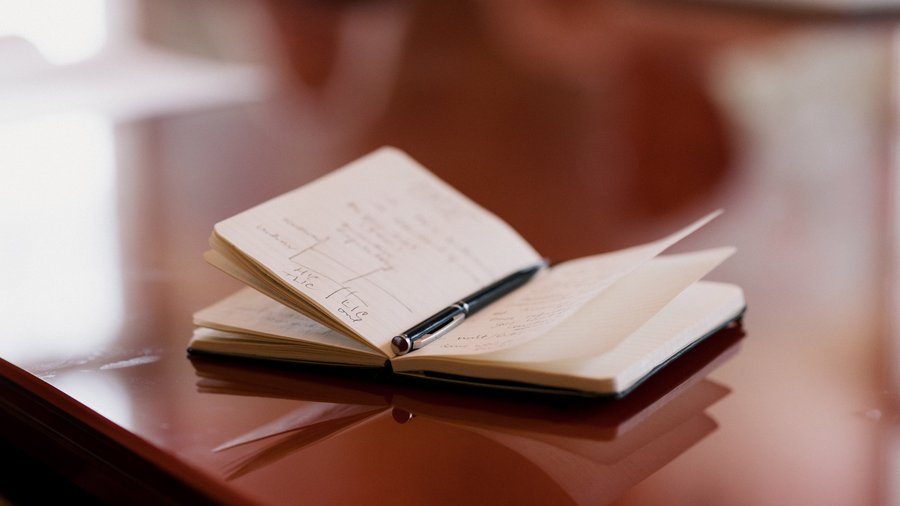 An image of an open notebook laying on a table with a pen inside