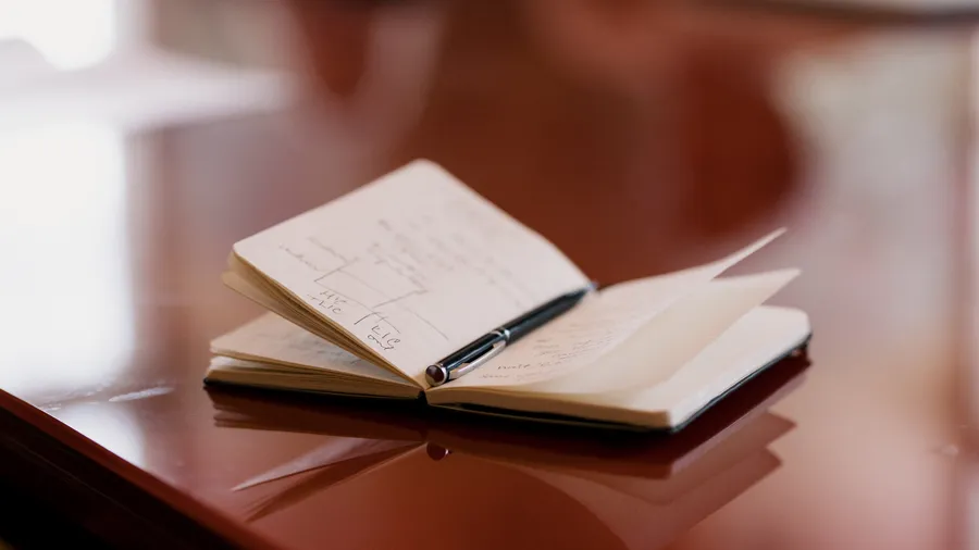 An image of an open notebook laying on a table with a pen inside