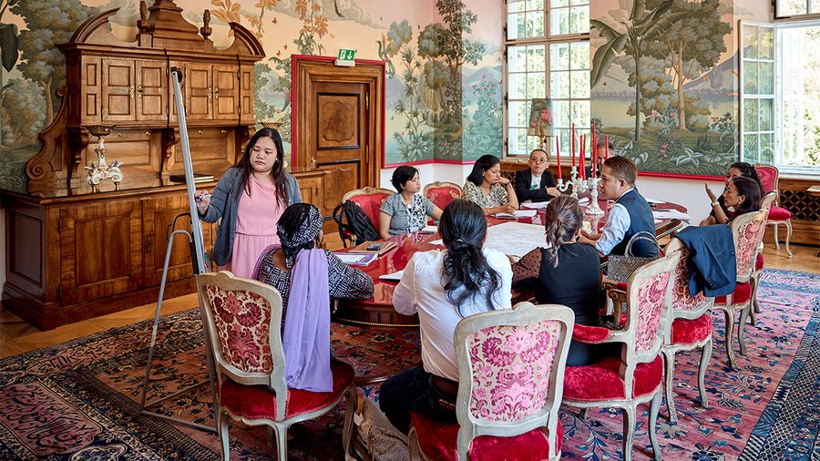 a group of people sitting around a table in the red salon of schloss leopoldskron