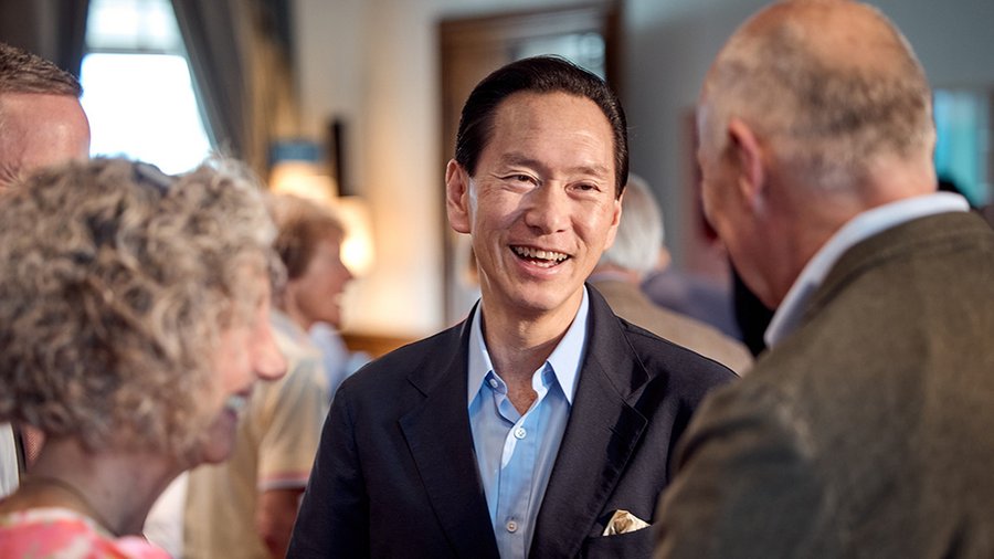 a man in a suit stands with a big smile while speaking with a man and woman