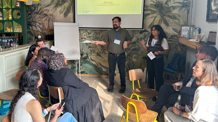 Two individuals stand in front of a crowd while presenting from a screen
