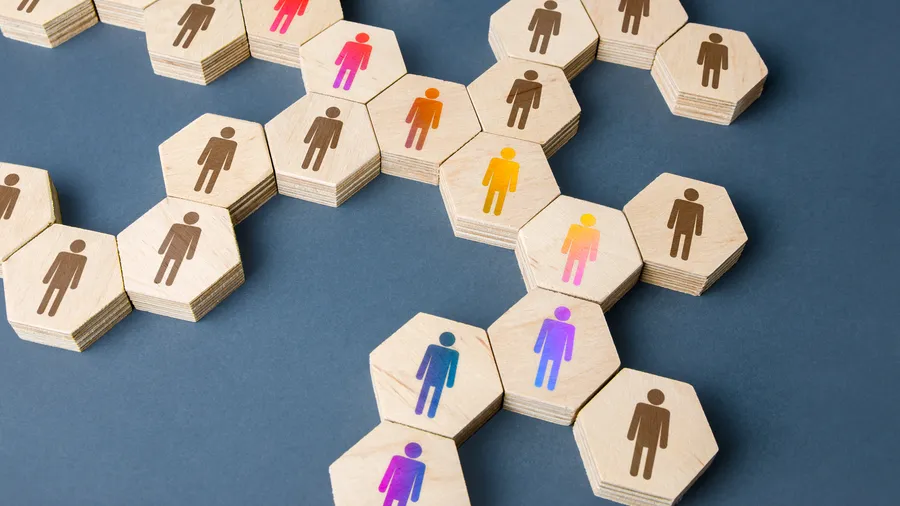 A network of wooden hexagonal blocks, each featuring an icon representing a person, are arranged on a blue-gray background. The blocks are connected in a pattern, with some icons colored in red, orange, yellow, and purple.