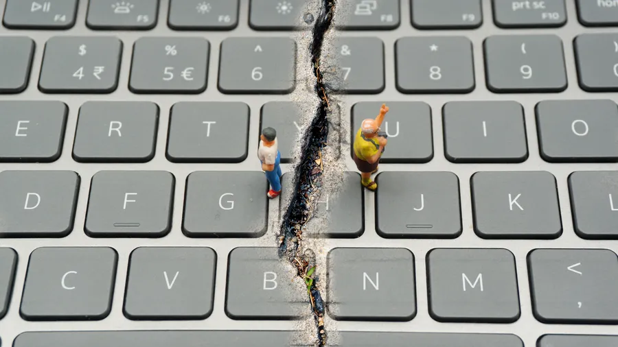 Split keyboard with two people facing away, representing internet confrontation, digital divide, social divide, and divided world conflicts.