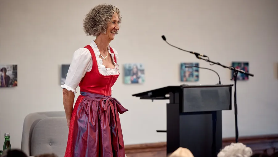 woman with curly grey hair in a dirndl speaks into a microphone