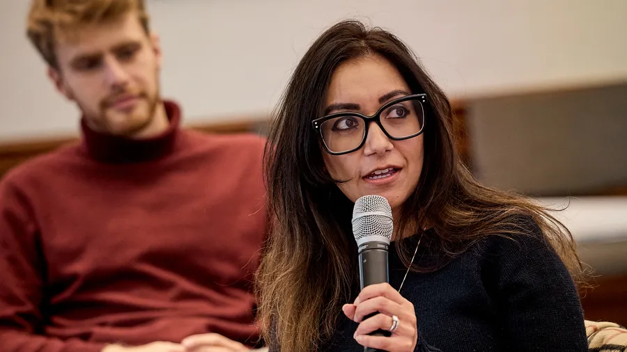 a woman speaks into a microphone and looks to the right 
