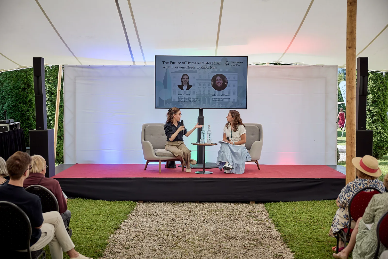 two women have a discussion on a stage in front of an audience