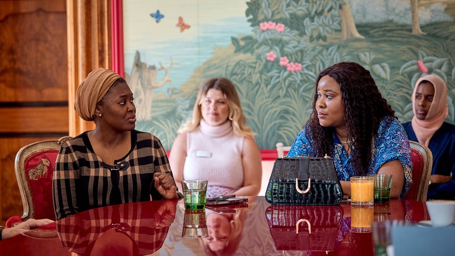 Two women sit at a table in discussion as two other women look on and listen