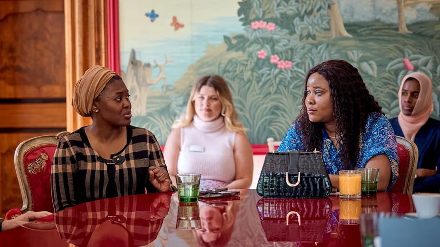 Two women sit at a table in discussion as two other women look on and listen