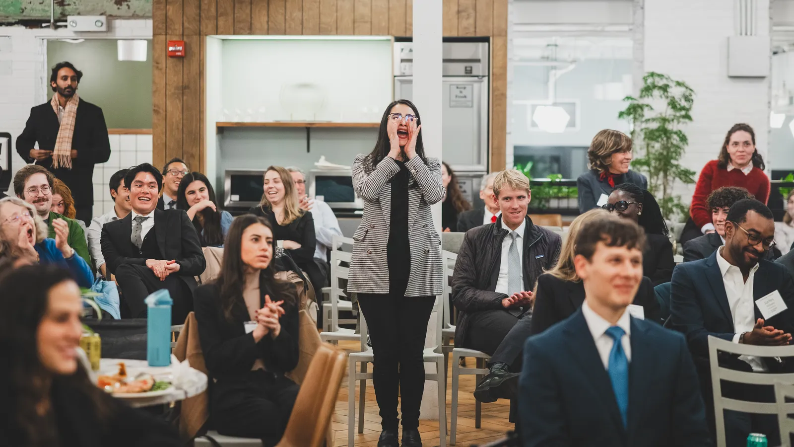 a woman stands in the midst of a seated crowd and appears to be shouting something