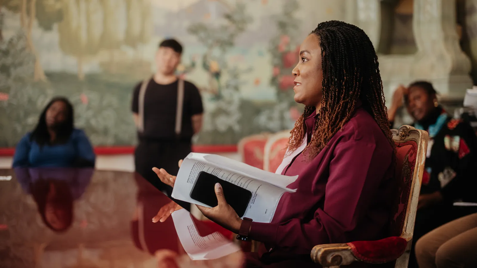 a woman sitting at a table and holding a notebook and looking into the distance off camera