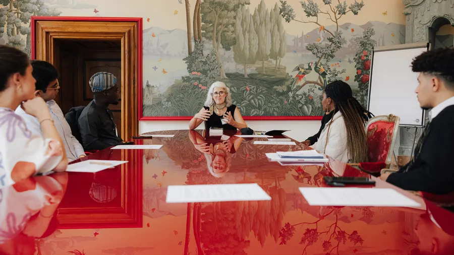 a diverse group of younger and older people sit around a table in the Red Salon of Schloss Leopoldskron during a Salzburg Global session
