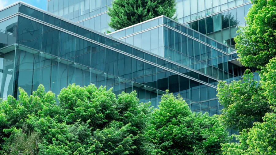 a photo of a modern glass city building surrounded by green plants