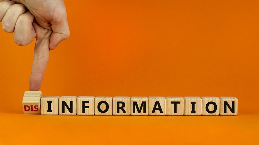 a photo of blocks with letters spelling disinformation, and someone's hand tipping over the prefix "dis"