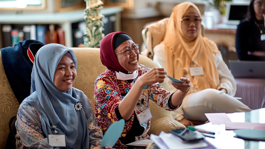 Three women sit at a table reading from a card and smiling