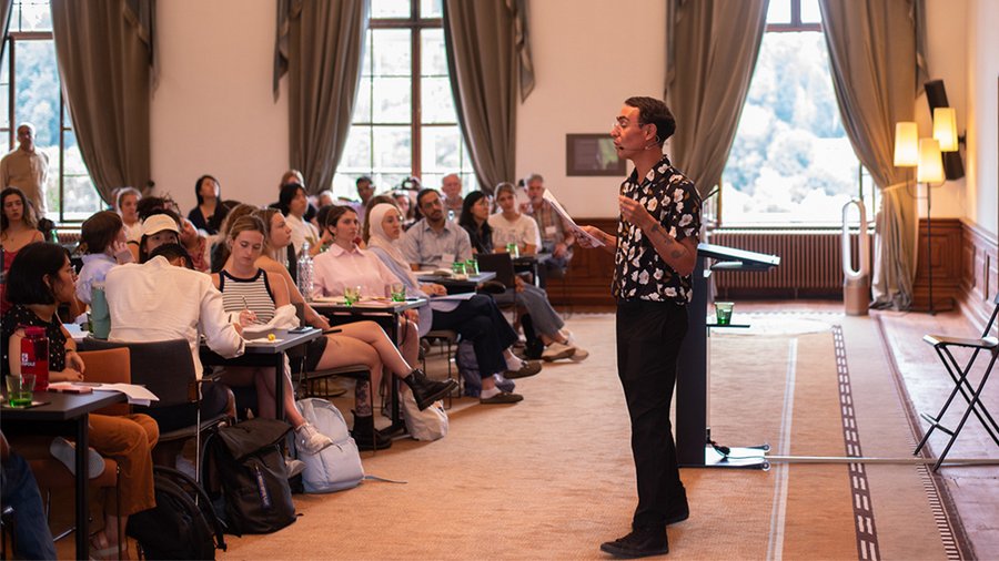 A man speaks in front of a group of young participants in the Gallery, a large room in Schloss Leopoldskron.