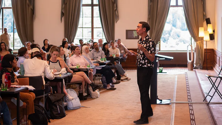 A man speaks in front of a group of young participants in the Gallery, a large room in Schloss Leopoldskron.