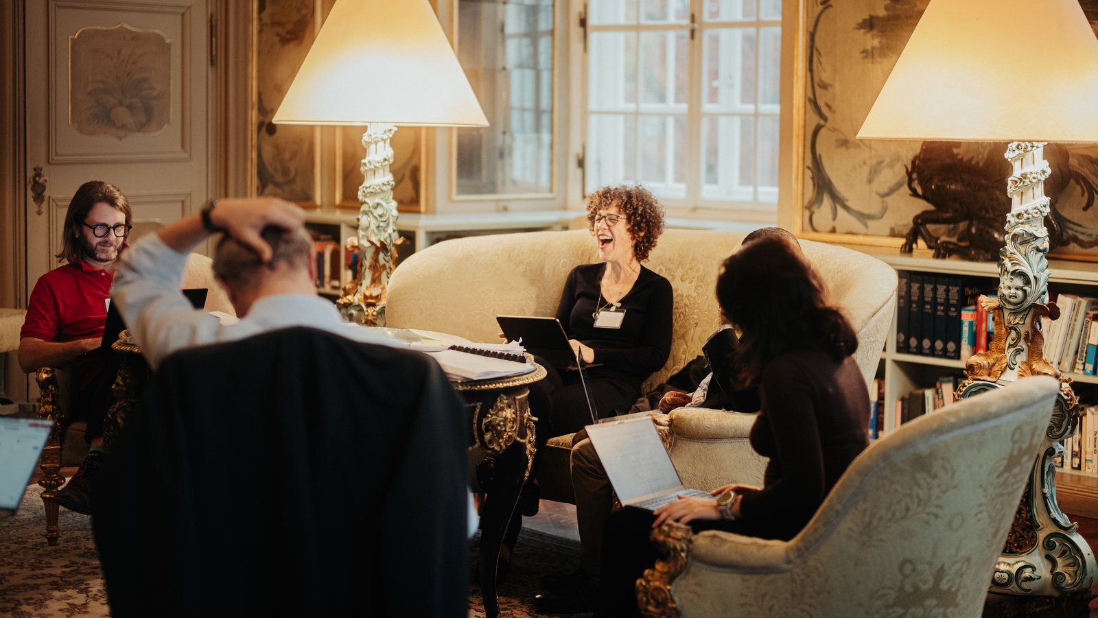 a woman sits laughing while discussing with a group in the Green Salon