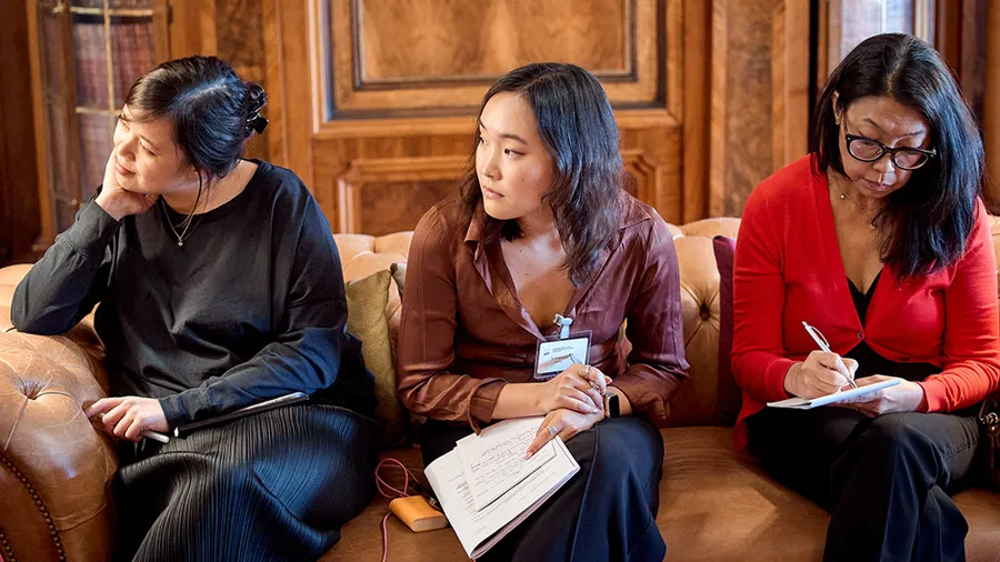 three women with dark hair sit on a couch and attentively look to the left.