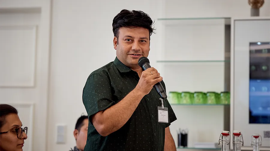 a man with dark hair speaks into a microphone and looks into the camera