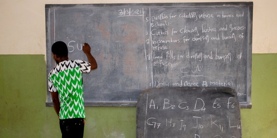 Opialu, Benue State - March 6, 2021: African Teacher Teaching His Students English Language in a Rural Community as they Pay Attention to his Explanations While Seated on a Wooden Bench