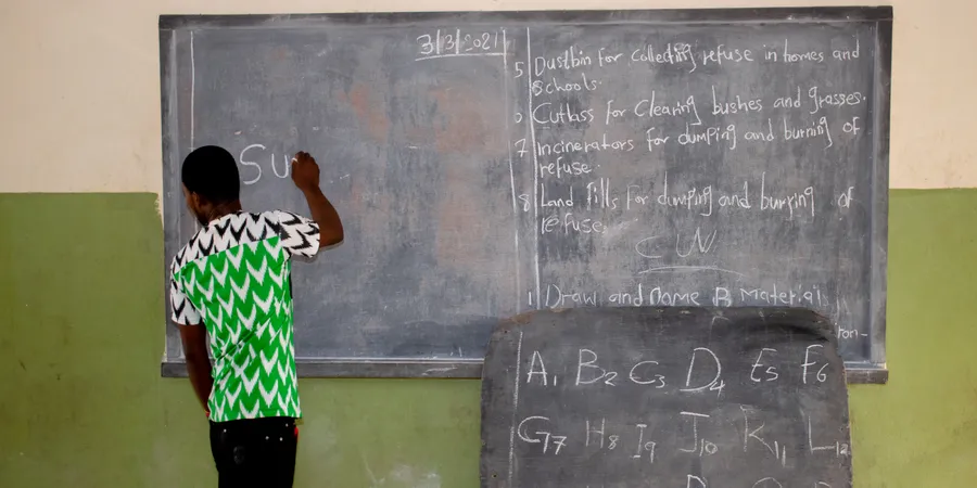Opialu, Benue State - March 6, 2021: African Teacher Teaching His Students English Language in a Rural Community as they Pay Attention to his Explanations While Seated on a Wooden Bench