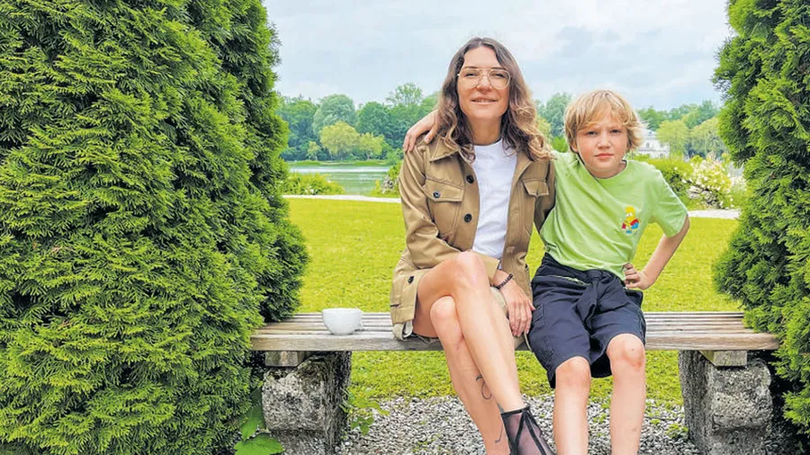 Tetiana Grynova, a woman with light hair, sits next to her son Dan on a bench surrounded by nature.