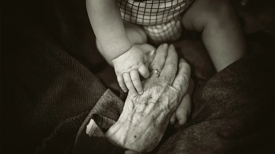 an image of an elderly hand holding the hand of an infant
