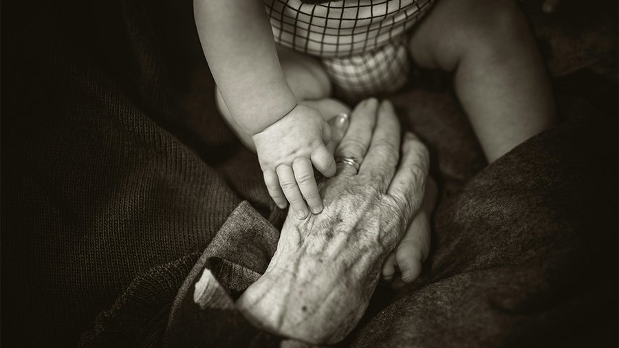 an image of an elderly hand holding the hand of an infant