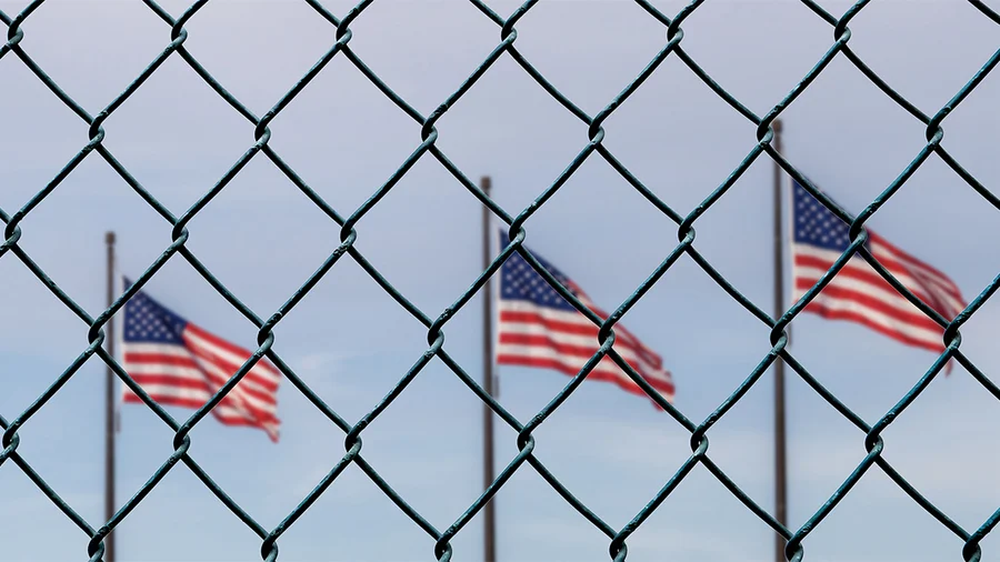 a row of three american flags behind a chain-link fence