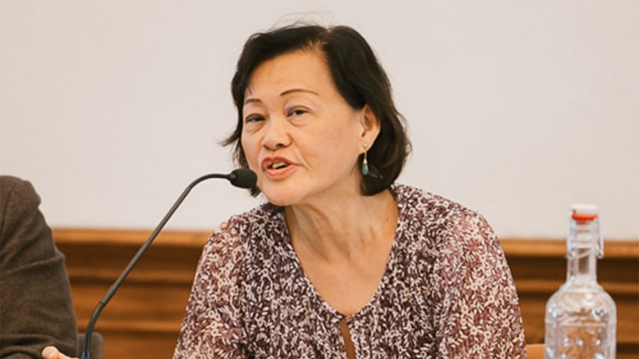A woman with dark hair speaks into a microphone