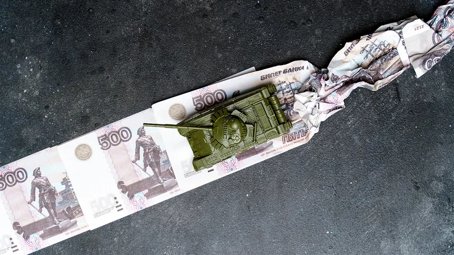 A green toy tank runs over a row of Russian rubles