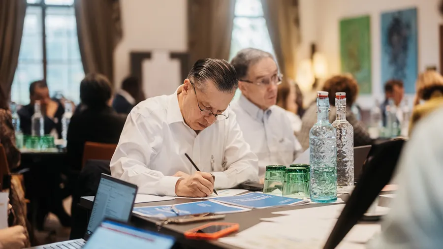 This image shows Gonzalo Canseco Gomez sitting down in Schloss Leopoldskron's Gallery and writing on a piece of paper.