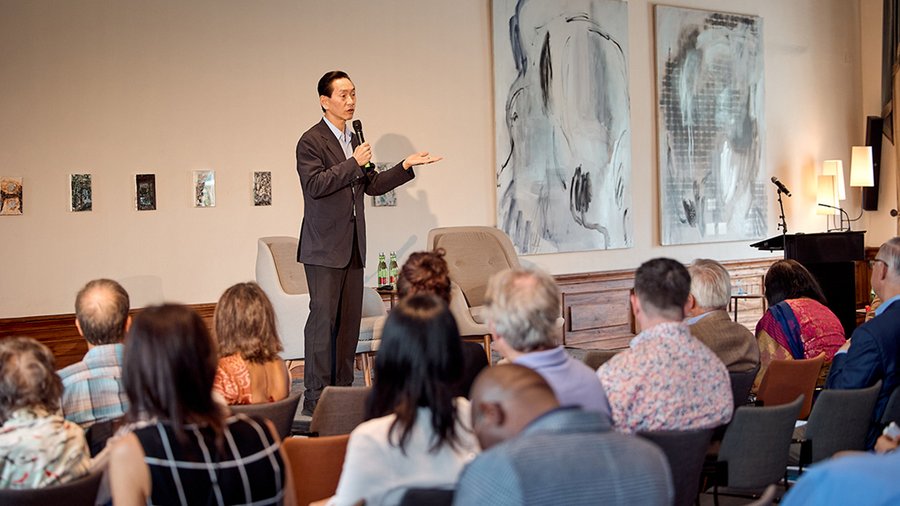A man stands speaking into a microphone in front of an audience.