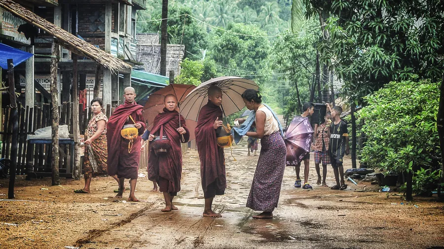 individuals are pictured on the street in myanmar as a woman hands money to young boys.