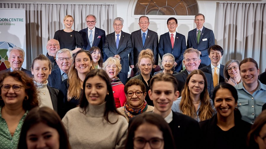 6 speakers stand in front of a crowd where everyone is smiling and facing the camera.