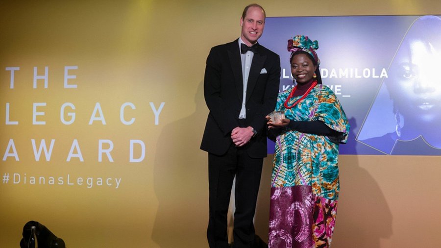 a man in a suit and a woman in a colorful dress stand smiling at the camera as the woman receives an award