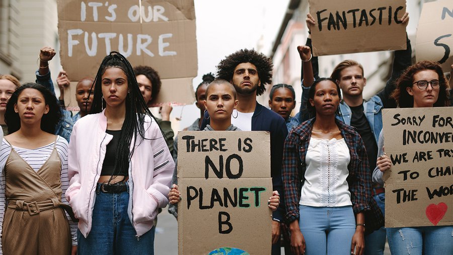 A diverse group of young climate activists hold handmade signs with environmental messages, including "There is No Planet B" and "It's Our Future," during a street protest.